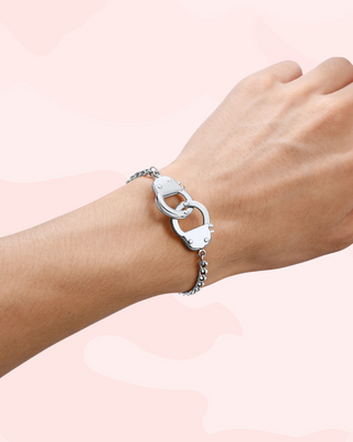 Silver handcuff bracelet on a wrist against a light pink background