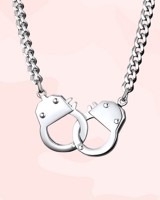 Silver handcuff-shaped pendant on a chain against a pink background