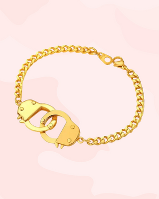 Gold bracelet with handcuff design on a pink background
