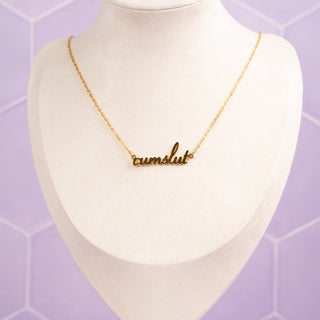 A gold cumslut necklace displayed on a mannequin, showcasing how it sits on the neckline.