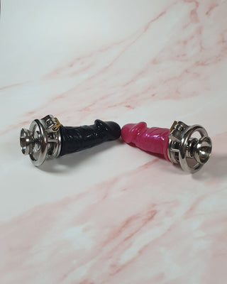 The pink and black Flat Gatling Thruster chastity cages shown lying together together. The cages are identical, but the dildo's are different colours.