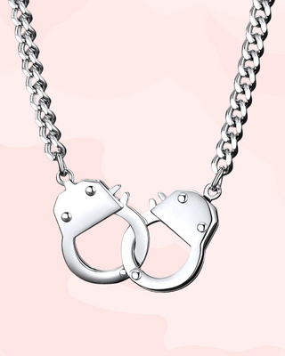 Silver handcuff-shaped pendant on a chain against a pink background
