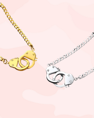 Two necklaces with handcuff pendants, one gold and one silver, on a pink background.