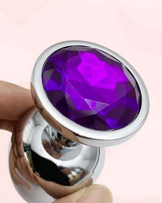 Purple gemstone in a silver setting held by a hand against a pink background