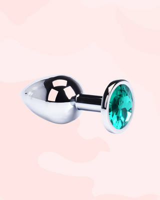 Metallic anal plug with a green gemstone on a light pink background