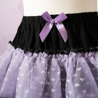 A close up of the see through fabric with heart embroidery, black waistband and decorative purple bow.