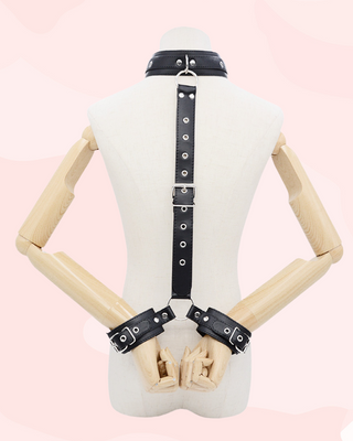 Mannequin wearing a black leather harness with neck collar and wrist cuffs on a pink background