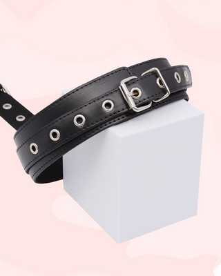 Black leather collar with silver buckles on a white block against a pink background