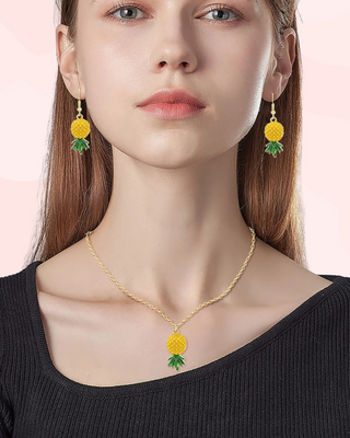Woman wearing a gold necklace and earrings with pineapple designs on a pink background