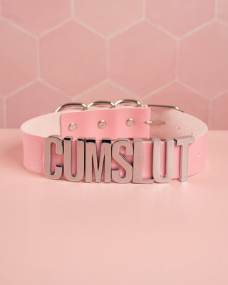 A picture of the cumslut collar in pink showing text on the front.
