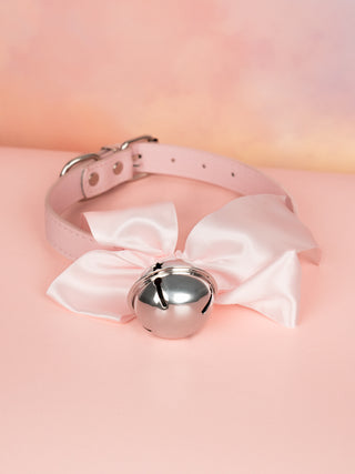 The pink Satin Soft Bow Collar lying on a pink surface alone, the large silver bell can be seen to the front.