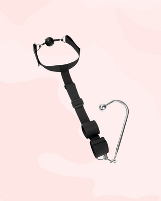 An angled view of the black Shadowbound Harness, you can see the ball gag, adjustable strap, wrist cuffs and anal hook.