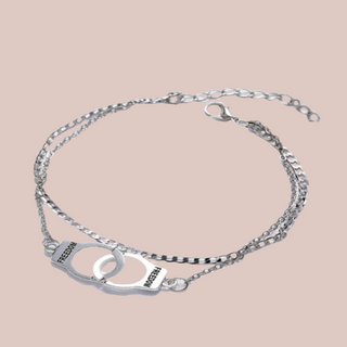 The silver handcuff ankle chain lying in a circular shape, how it wraps around the ankle. You can see the freedom detailing on the handcuffs