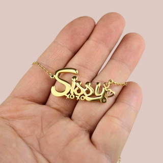 A close up of the gold Sissy necklace on a hand, it is shown  with xoxo beneath and hearts at the end.