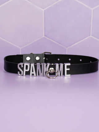 The black slimline Spank Me choker can be seen with its centre O-ring which allows the collar to be attached to a lead.