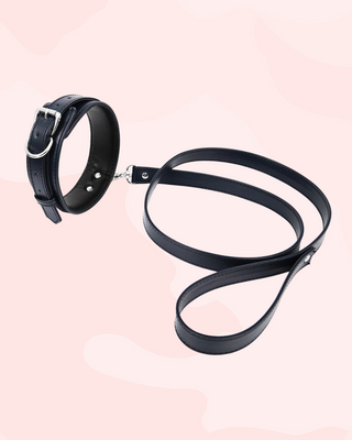 Black leather collar and leash set on a light pink background