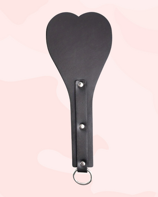 Black paddle with a heart-shaped head on a pink background