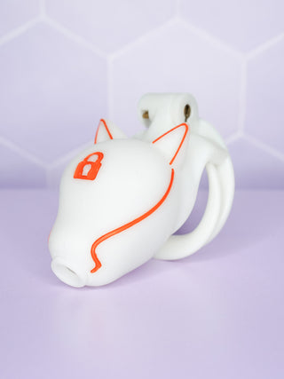 An angled view of the fully assembled chastity cage, the white cage with orange detailing can be seen, as can the orange lock to the wolf's head.