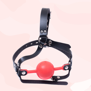 Black leather head gag with a red ball on a pink background