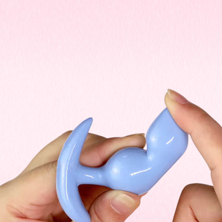A light blue anal expander held between two hands against a solid light pink background
