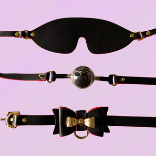 A close up of the eye mask, ball gag and collar, they are shown on a purple background
