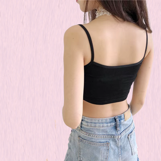 A woman shown from the back wearing a black spaghetti-strap crop top and light-wash blue jeans, standing against a light pink textured wall.