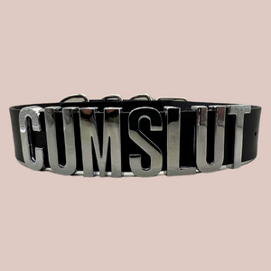 A close up view of the Cumslut collar, you can see the silver shiny lettering that is all in capital letters. There is matching silver buckles at the back.