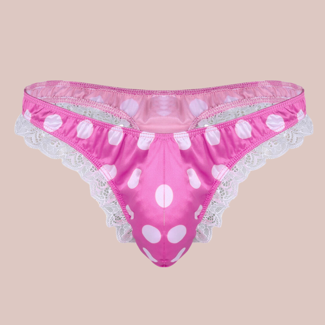 A bright pink satin men's female style knickers. They have a white spot pattern on the bright pink fabric, white lace edging to the legs and a thong style back.