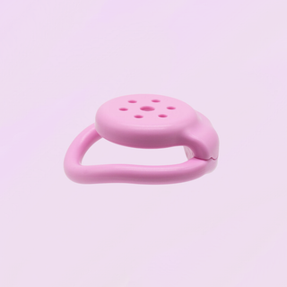 A side view of the chastity cage in pink, it is shown on a soft pink background