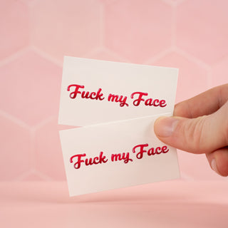 Showing two identical Fuck My Face temporary tattoos in front of a pink background