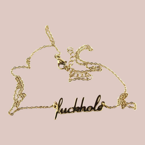 The fuckhole necklace is shown laying on a flat surface, you can see that there is a good length to the chain and the lettering a decent size.