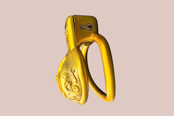 A side view of the Gold Ornate Scroll Sissy Pussy chastity cage from House Of Chastity, you can see it here fully assembled with the 48mm base ring ring and integral lock fitted.