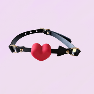 the black strap gag with arrow, it is accented with gold hardware and a red heart ball gag.