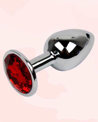 Metallic anal plug with red gemstone on a pink background
