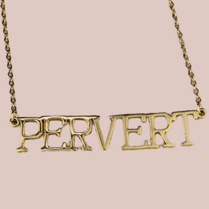 A close up view of the Pervert necklace, you can see the captial letters, gold colouring and the chain.