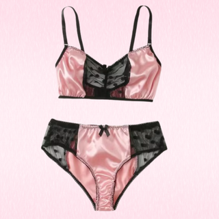 A two-piece lingerie set featuring a satin bralette and matching panties in pink and black, displayed on a light pink textured background.