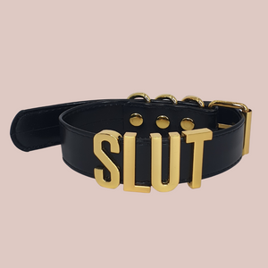 A close up of The Slut collar, it has a black collar with gold lettering and fastenings.