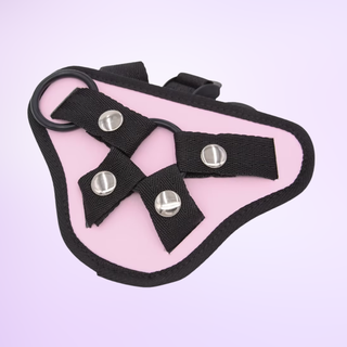 A flat view of the pink and black harness it is shown on a purple background, one of the rubber rings can be shown clipped in.