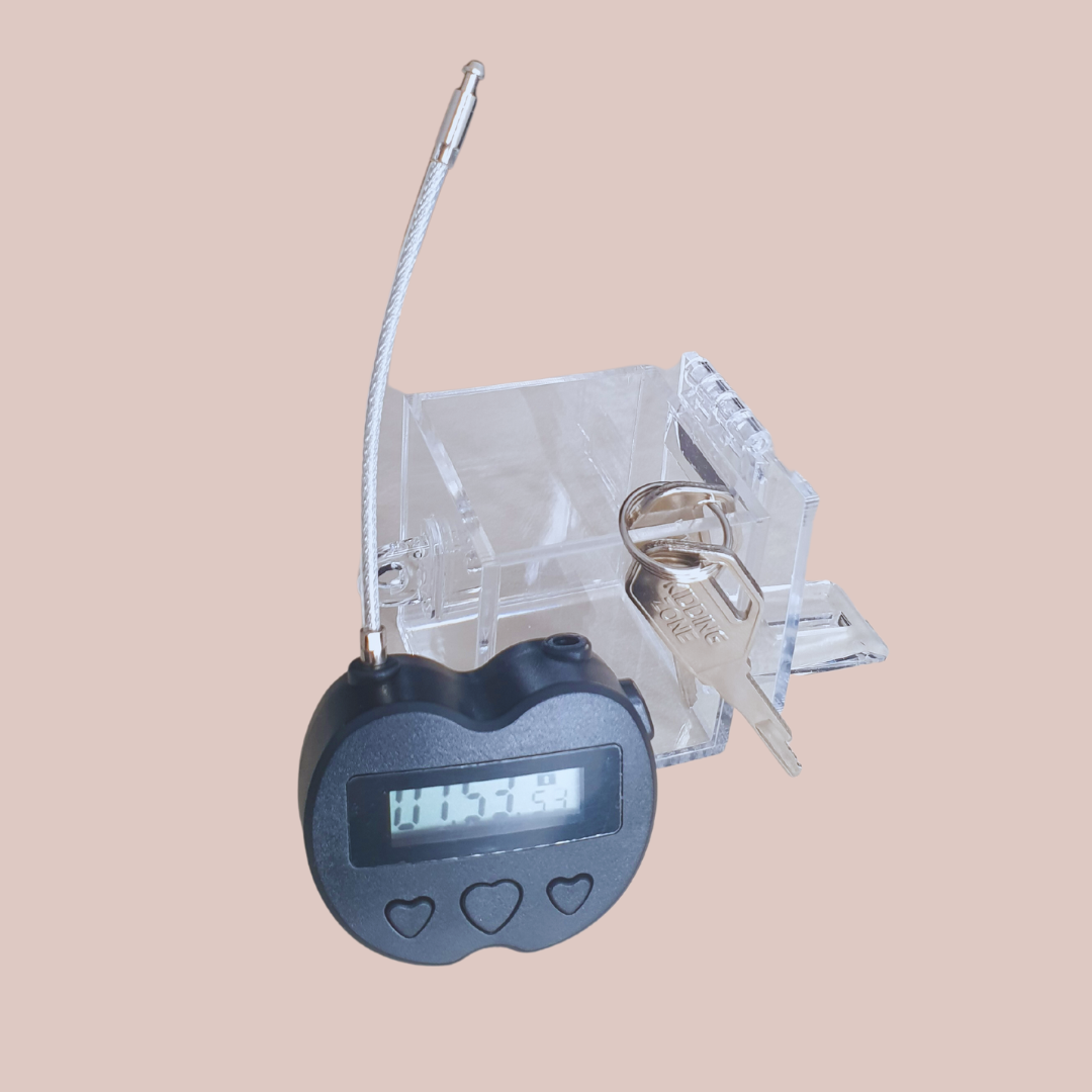 Showing the clear chastity key safe box, where you can see your chastity cage keys locked away nice and tight and you can't get to them. Also shown is the electronic lock that can be set on a timer for release.