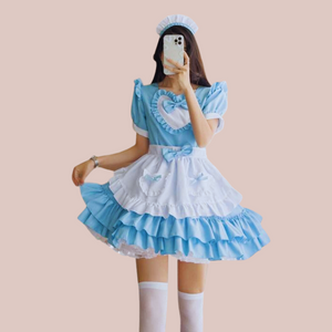 The Florence flouncy maid dress shown in full length. You can see the two tone colouring of blue and white, the frills to the shoulder, around the heart shaped bodice design and double layer frills to the skirt. There are decorative bows to the heart waist band and pockets.