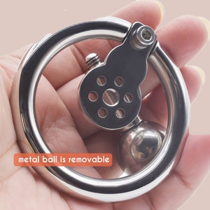 Shown in the palm of a hand, The Negative Enslavement chastity device has a removable urethral tube and ball and are shown removed from the device.