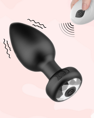 Black anal plug with clear jewelled base stone, with on off button in the centre of the gem, and the remote control pad that allows the anal plug to be controlled.