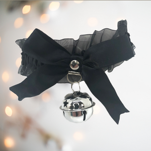 A satin and gauze fabric choker / necklace that has a matching satin bow to the front, with a large hanging bell. There are ribbon string ties to the back, allowing for different sized necks and it comes in soft black.