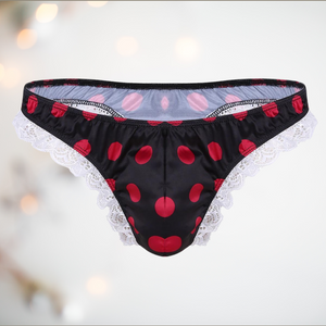 A black satin men's female style knickers. They have a red spot pattern on the black fabric, white lace edging to the legs and a thong style back.