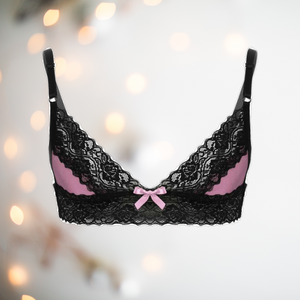Sized for men to wear, this is a pale pink bralette that has pale pink cups with black lace edging to the top of the cup and a band of black lace that runs from front to back at the bottom of the bra. It has two adjustable thin black straps and fastens at the back.