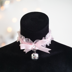 A delicate pink satin and gauze choker with large bow design to the front and silver bell decoration. This choker is fixed by tie strings at the back.